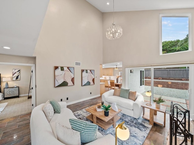 living area featuring a notable chandelier, baseboards, visible vents, wood finished floors, and a high ceiling
