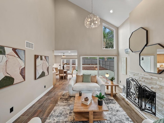 living room featuring a fireplace with raised hearth, baseboards, visible vents, a chandelier, and high vaulted ceiling