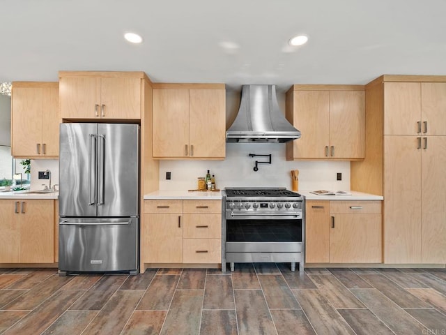 kitchen featuring light brown cabinets, recessed lighting, premium appliances, wall chimney range hood, and light countertops
