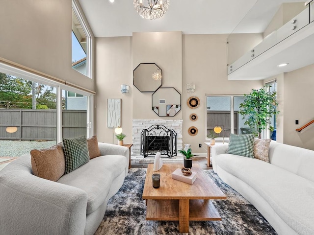 living area featuring a fireplace with raised hearth, a healthy amount of sunlight, an inviting chandelier, and a towering ceiling