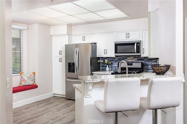 kitchen featuring stainless steel appliances, baseboards, a peninsula, a sink, and decorative backsplash