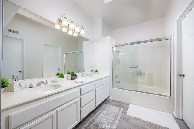 bathroom featuring double vanity, bath / shower combo with glass door, and wood finished floors