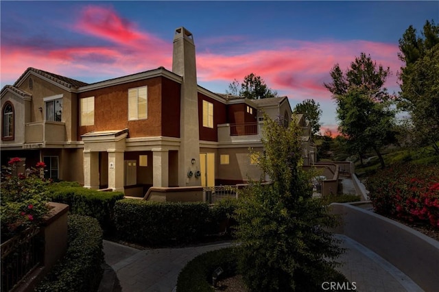 view of front of house featuring a balcony, stucco siding, and a chimney