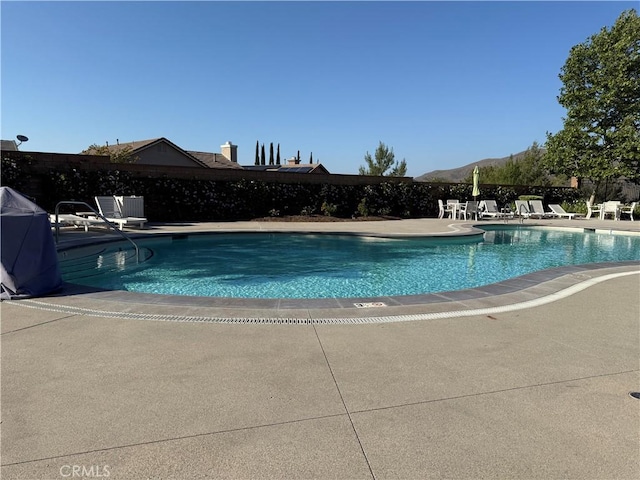 community pool with a patio area, fence, and a mountain view