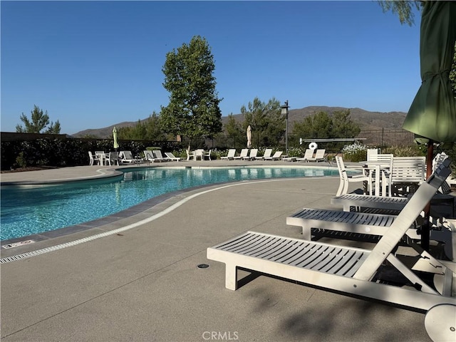 community pool with a mountain view, a patio area, and fence