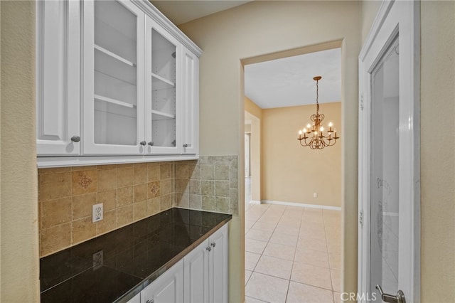 kitchen featuring white cabinets, light tile patterned flooring, glass insert cabinets, a chandelier, and tile counters