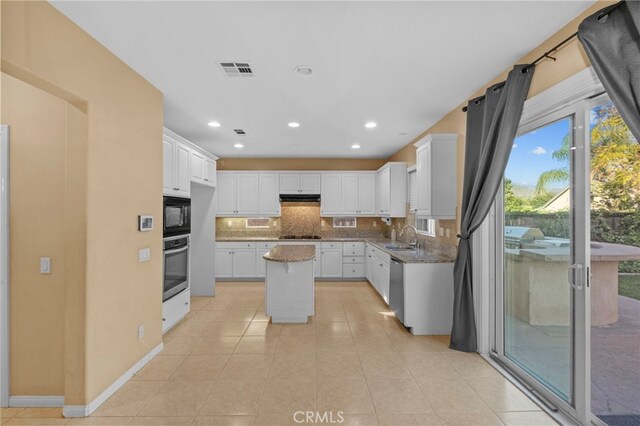 kitchen with stainless steel appliances, a sink, tasteful backsplash, under cabinet range hood, and a center island