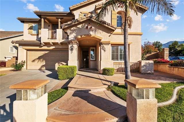 mediterranean / spanish-style house with a balcony, stucco siding, an attached garage, a tiled roof, and concrete driveway