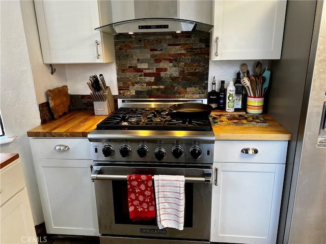 kitchen featuring butcher block counters, white cabinetry, backsplash, wall chimney range hood, and stainless steel appliances