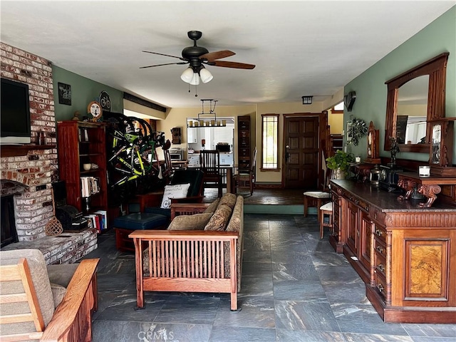 living room featuring a ceiling fan, a brick fireplace, and stone finish flooring