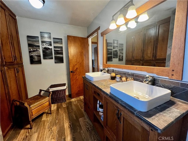 full bathroom featuring a sink, double vanity, tasteful backsplash, and wood finished floors