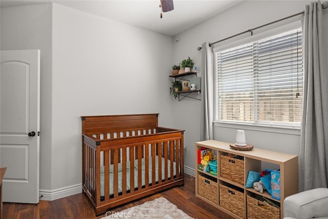 bedroom featuring a nursery area, a ceiling fan, wood finished floors, and baseboards