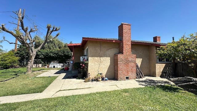 view of home's exterior with a yard, fence, stucco siding, and a chimney