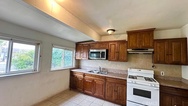 kitchen with under cabinet range hood, light tile patterned floors, stainless steel microwave, a sink, and gas range gas stove
