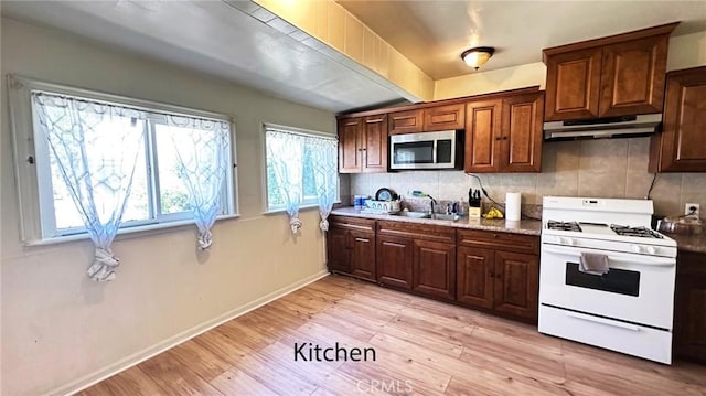 574 Davidson Ln, Pomona, CA 91768 - kitchen featuring white range with gas stovetop, stainless steel microwave, under cabinet range hood, a sink, and backsplash