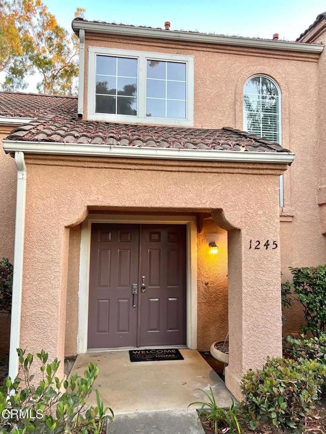 view of exterior entry with a tile roof and stucco siding