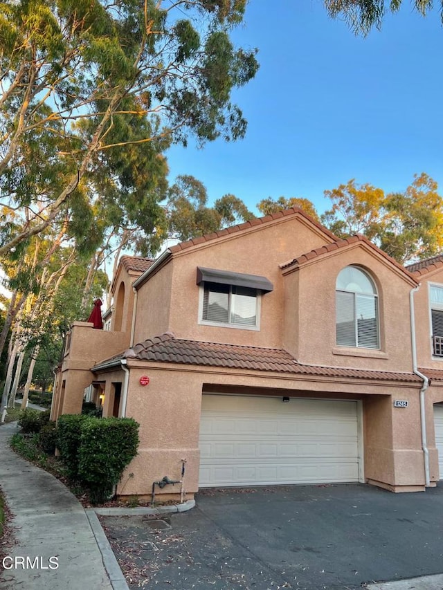 view of front of property featuring stucco siding, a garage, a tiled roof, and aphalt driveway