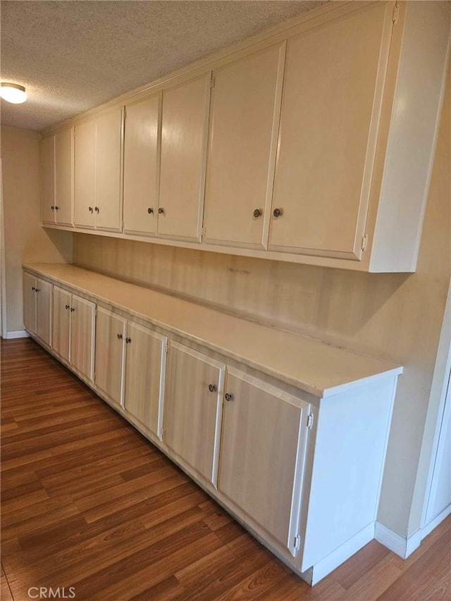 interior space featuring baseboards, light countertops, a textured ceiling, and wood finished floors