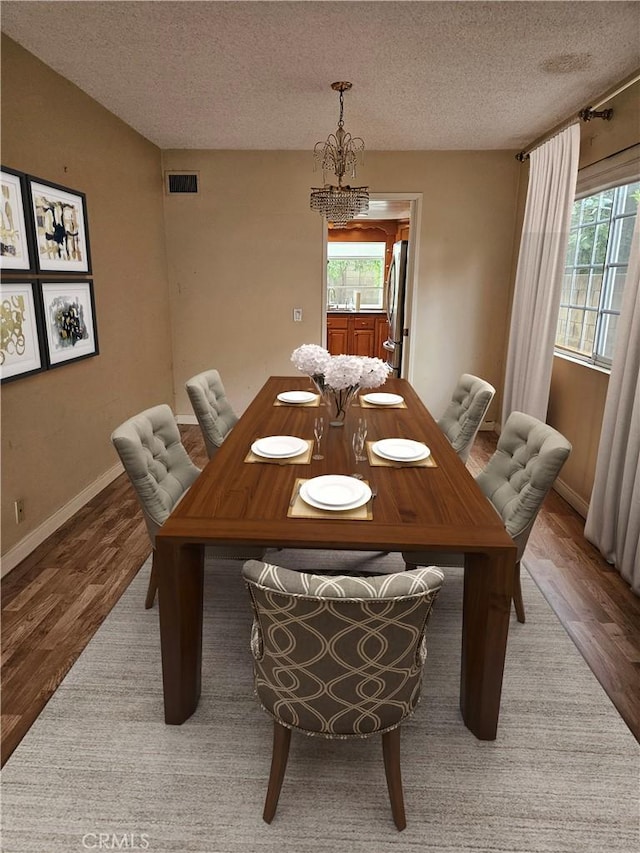 dining space with a textured ceiling, visible vents, plenty of natural light, and wood finished floors