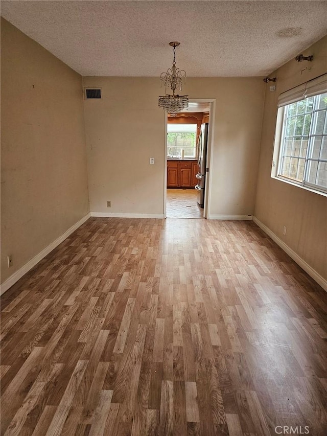 unfurnished dining area featuring wood finished floors, a textured ceiling, visible vents, an inviting chandelier, and baseboards