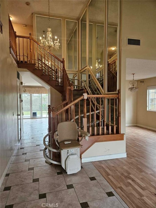 unfurnished living room with stairs, visible vents, a towering ceiling, and a notable chandelier