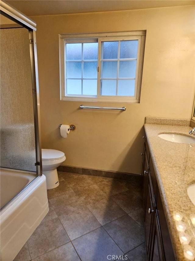full bath featuring double vanity, toilet, combined bath / shower with glass door, a sink, and baseboards