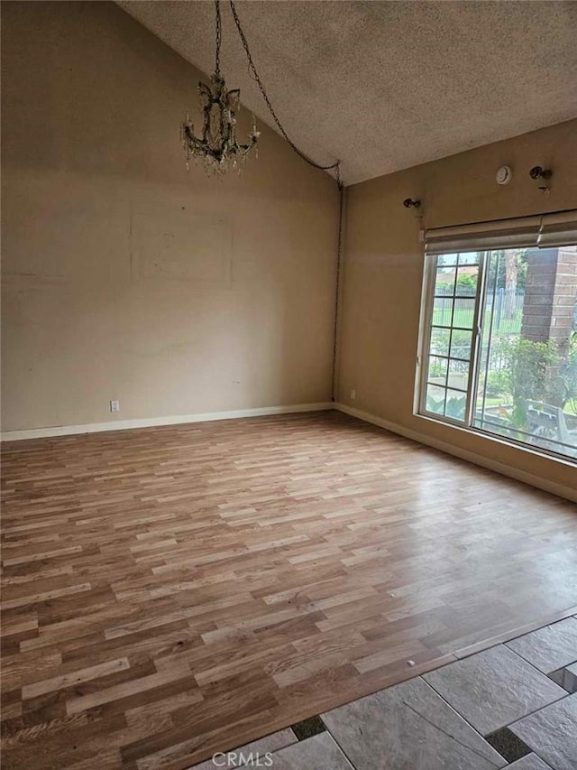 empty room featuring vaulted ceiling, a textured ceiling, a notable chandelier, and wood finished floors