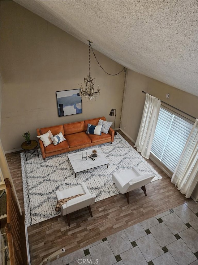 living area featuring lofted ceiling, a textured ceiling, baseboards, an inviting chandelier, and wood finished floors