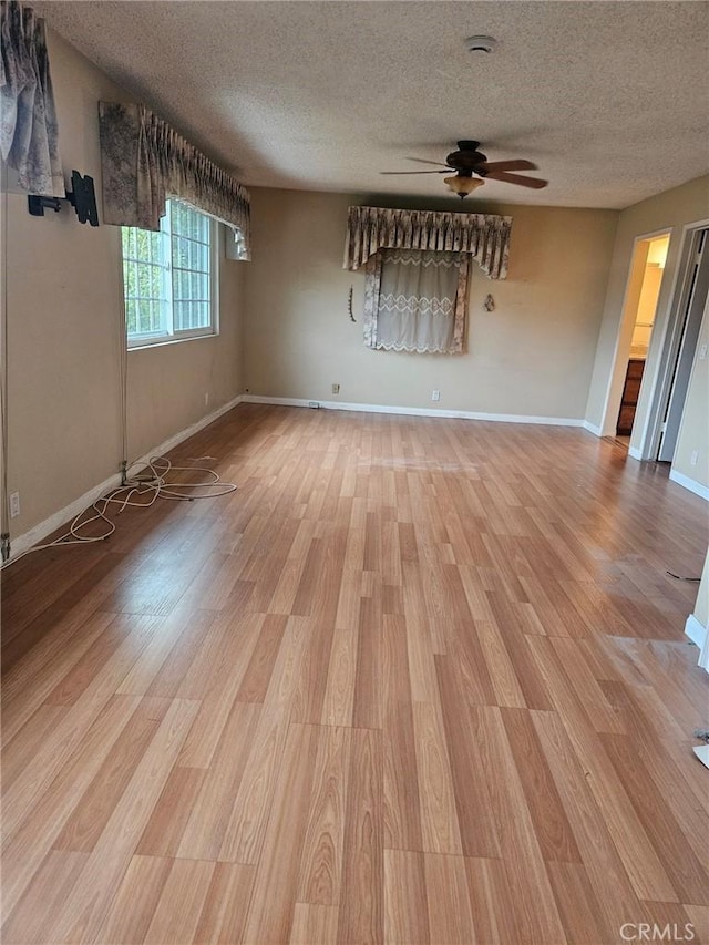 spare room with light wood finished floors, a textured ceiling, baseboards, and a ceiling fan