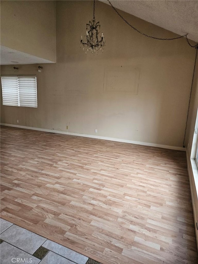 unfurnished room featuring a textured ceiling, high vaulted ceiling, a chandelier, baseboards, and light wood-style floors