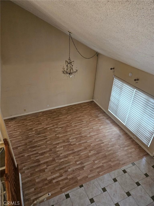 unfurnished dining area with wood finished floors, a textured ceiling, baseboards, a chandelier, and lofted ceiling