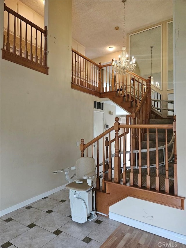 staircase featuring an inviting chandelier, a textured ceiling, visible vents, and baseboards