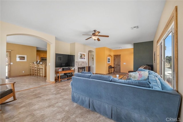 living area featuring visible vents, a fireplace, a ceiling fan, and arched walkways