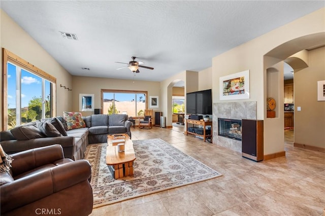 living room with light tile patterned floors, a fireplace, visible vents, ceiling fan, and arched walkways