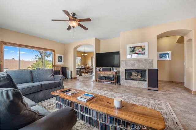 living area featuring a fireplace, arched walkways, a ceiling fan, and baseboards