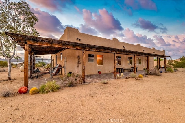 back of property at dusk with a patio area, a gate, and stucco siding