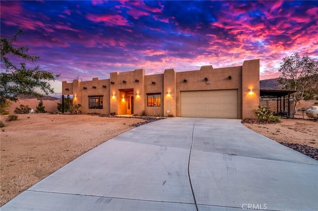 pueblo revival-style home with an attached garage, stucco siding, and driveway