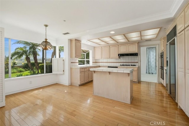 kitchen featuring tile countertops, a center island, black stovetop, under cabinet range hood, and a chandelier