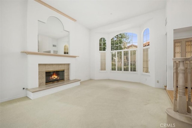 unfurnished living room featuring carpet floors, a tiled fireplace, and baseboards