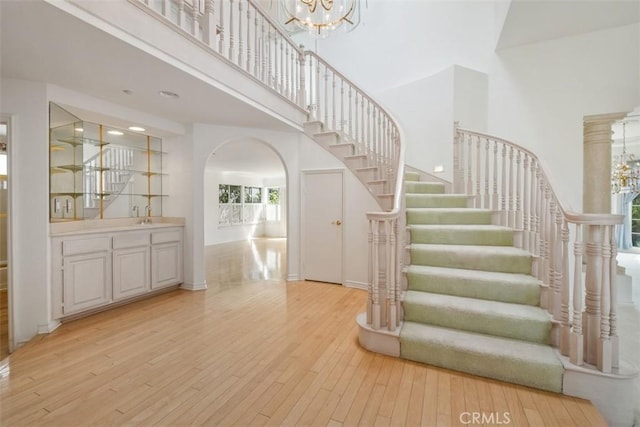 staircase featuring arched walkways, a chandelier, a towering ceiling, hardwood / wood-style floors, and baseboards