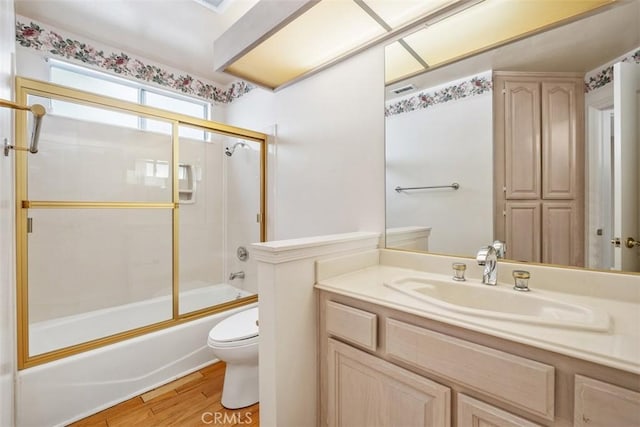 bathroom featuring toilet, wood finished floors, shower / bath combination with glass door, and vanity