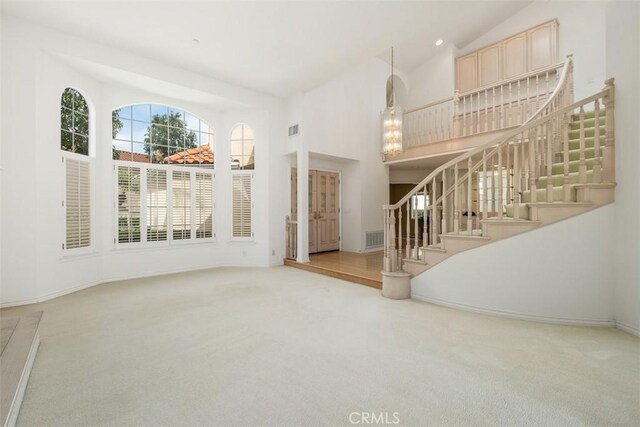 unfurnished living room with high vaulted ceiling, carpet flooring, stairs, and baseboards