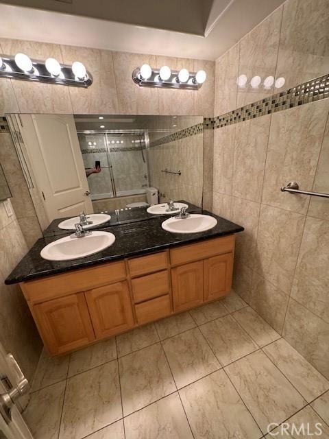 full bathroom featuring a sink, double vanity, tile walls, and a tile shower