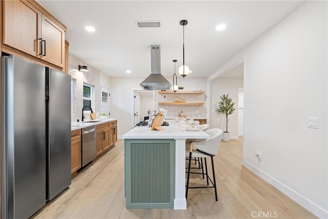 kitchen featuring visible vents, a sink, a kitchen bar, island exhaust hood, and stainless steel appliances