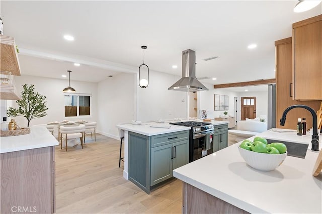 kitchen featuring a sink, island exhaust hood, open floor plan, stainless steel range with gas stovetop, and light wood-style floors