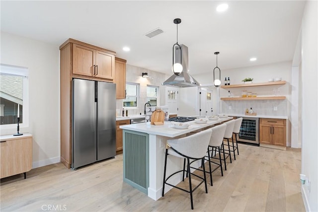 kitchen with light wood finished floors, wall chimney exhaust hood, beverage cooler, and appliances with stainless steel finishes