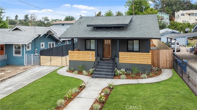 bungalow-style home with covered porch, fence private yard, a shingled roof, and a front lawn