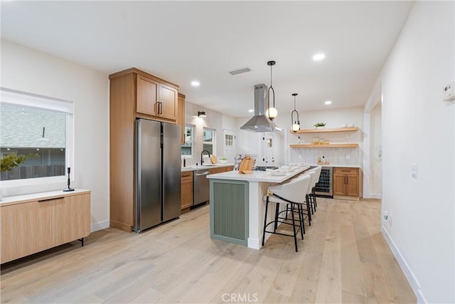 kitchen featuring exhaust hood, open shelves, light wood finished floors, a kitchen bar, and appliances with stainless steel finishes
