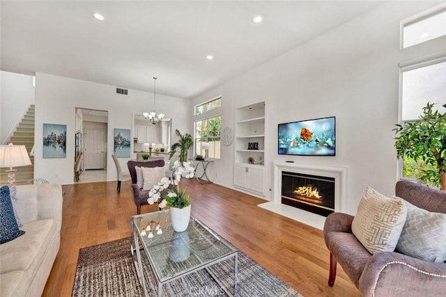 2516 Lewis Dr, Tustin, CA 92782 - living area featuring a chandelier, built in shelves, stairs, a glass covered fireplace, and light wood-style flooring