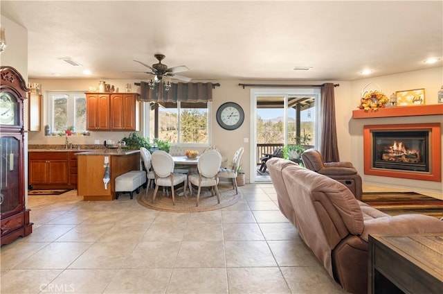 interior space featuring light tile patterned flooring, a lit fireplace, ceiling fan, and plenty of natural light